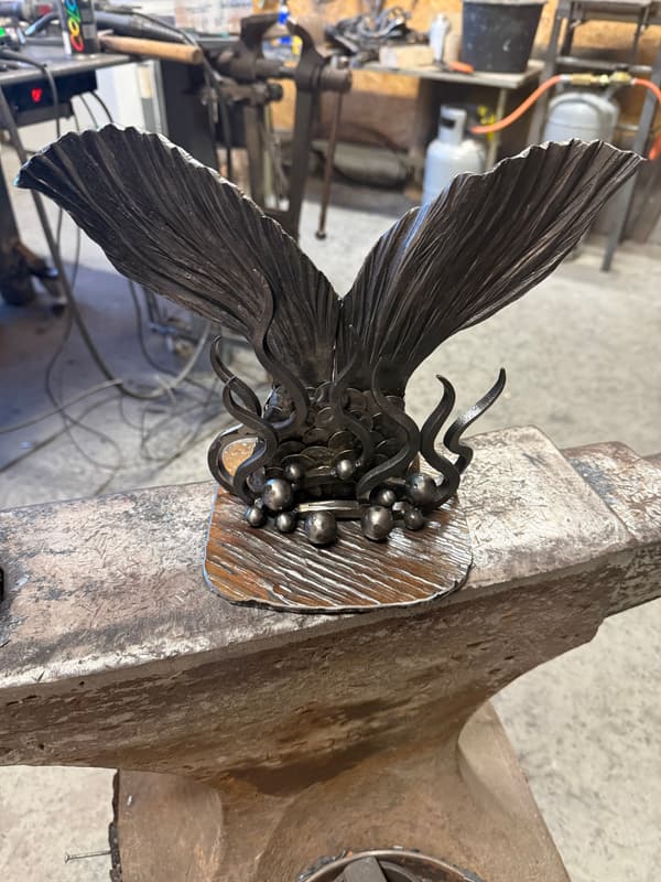 Smidd skulptur med to vinger på ambolten